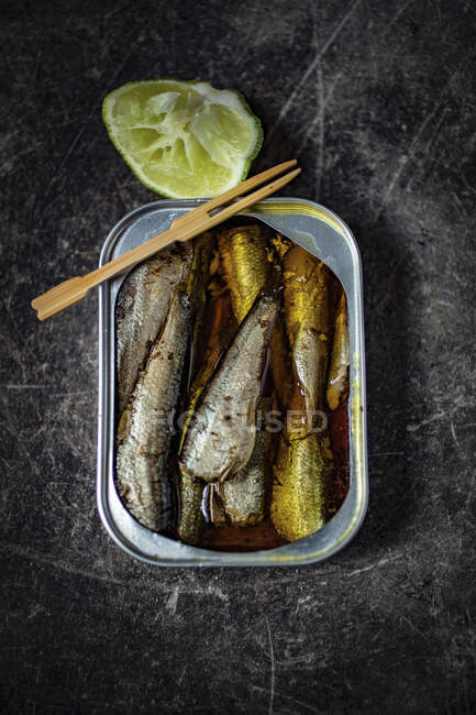 Sardinas en lata con tenedor de madera y lima - foto de stock