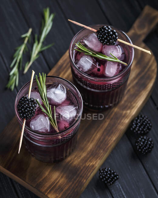 Cocktails with rosemary and blackberries in glasses on wooden board — Stock Photo