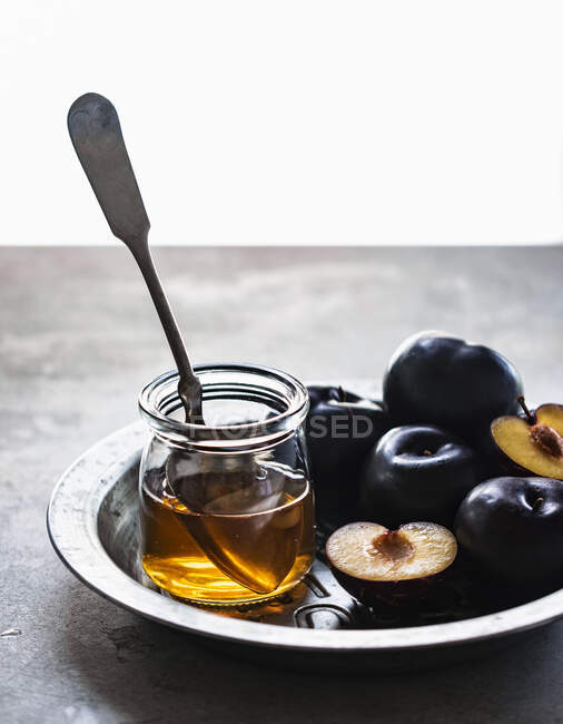Fresh plums and honey in jar with spoon — Stock Photo