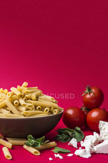 Un arreglo de pasta de penne, tomates, queso y hierbas - foto de stock