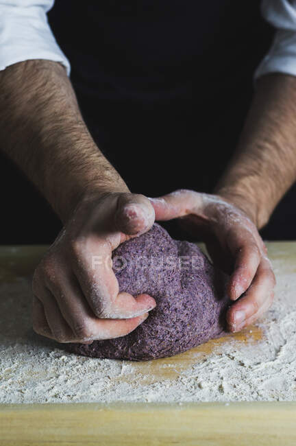Ein Mann knetet einen lila Brotteig auf einer bemehlten Holzoberfläche — Stockfoto