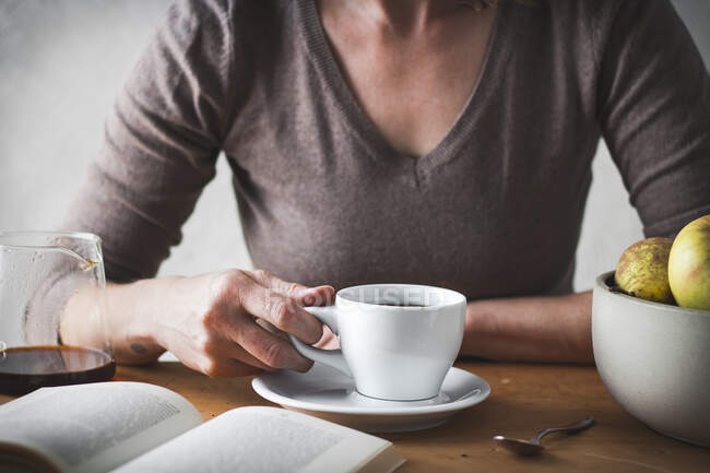 Mano de mujer con una taza de café y un libro - foto de stock