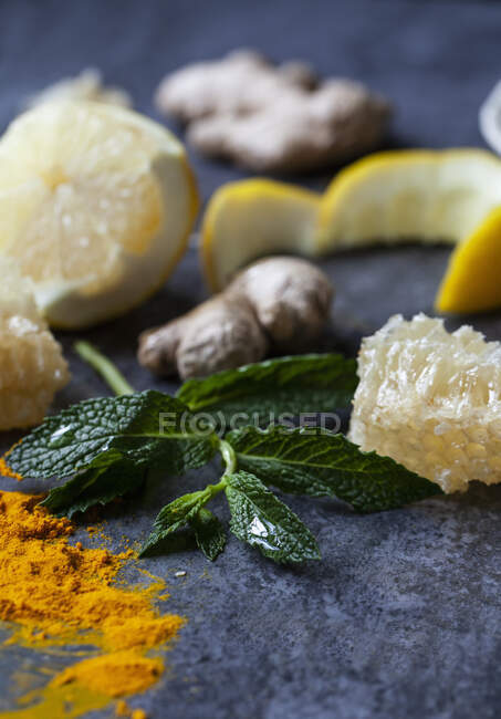 Limón, jengibre, cúrcuma en polvo, panal y menta en una superficie azul - foto de stock