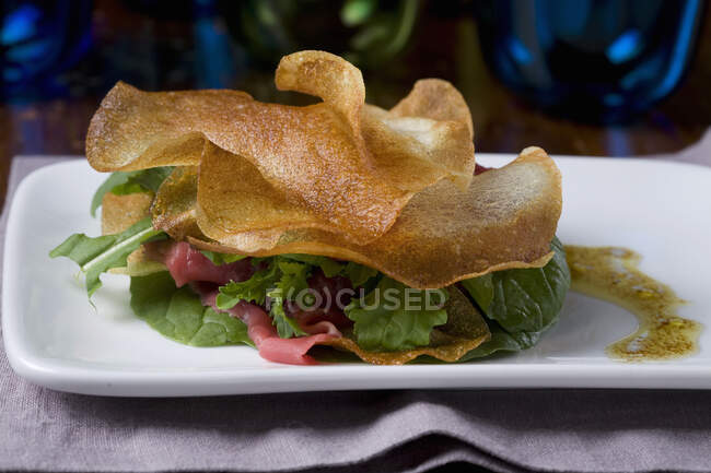 Un sándwich crujiente de patata con carpaccio de ternera, lechuga y vinagreta - foto de stock