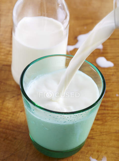 Milk pouring in glass on wooden surface — Stock Photo