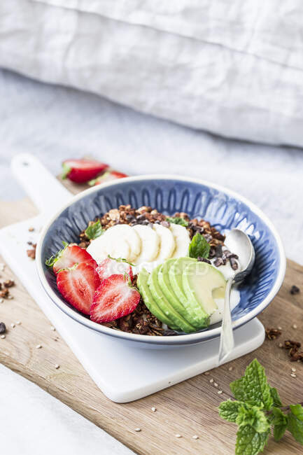 Almond and sesame seed granola with strawberries and avocado on a wooden board on a bed — Stock Photo