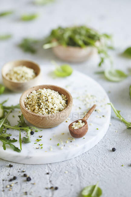 Peeled hemp seeds in a wooden bowl on a marble plate next to arugula leaves — Stock Photo