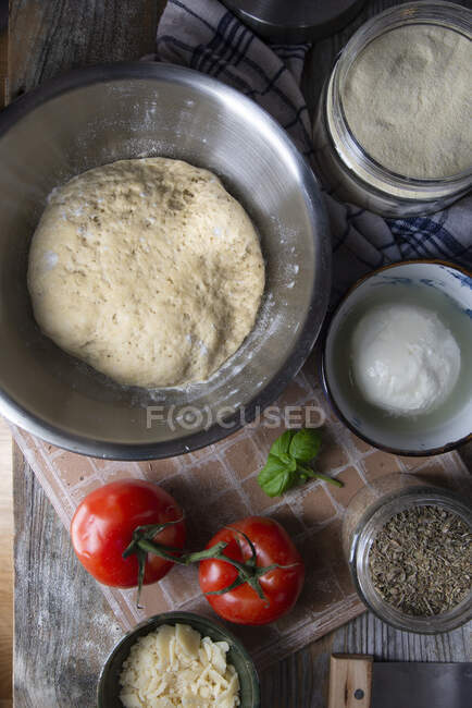 Pâte à pizza dans un bol en acier inoxydable et ingrédients pour pizza végétarienne — Photo de stock