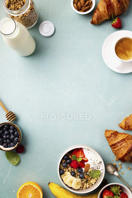 Colazione con muesli, yogurt, miele, banane fresche, frutti di bosco, semi di chia in ciotola, caffè e croissant — Foto stock