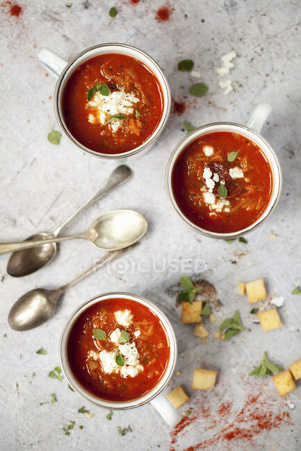 Copos de esmalte com sopa de tomate fumado coberto com feta e ervas — Fotografia de Stock