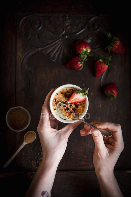 Hands holding Creme Brulee dessert with strawberries and spoon — Stock Photo
