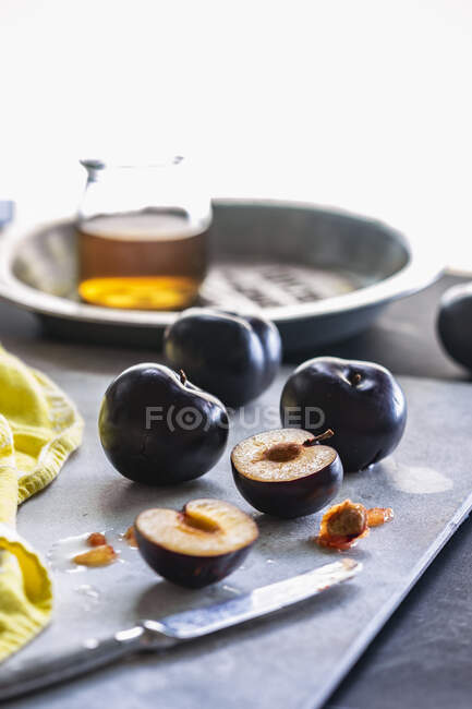 Prunes fraîches entières et coupées en deux sur la table avec couteau — Photo de stock