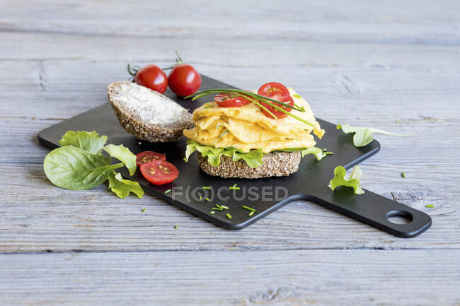 Un panecillo con huevos revueltos, ensalada y tomates - foto de stock