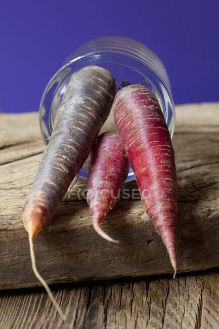 Red and purple carrots in glass on wooden surface — Stock Photo