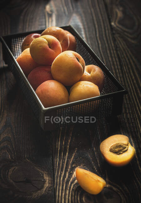 Abricots dans panier métallique et sur table en bois — Photo de stock