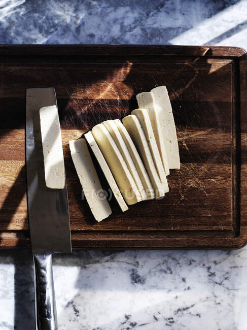 Slicing fresh pressed tofu on a dark wooden board — Stock Photo