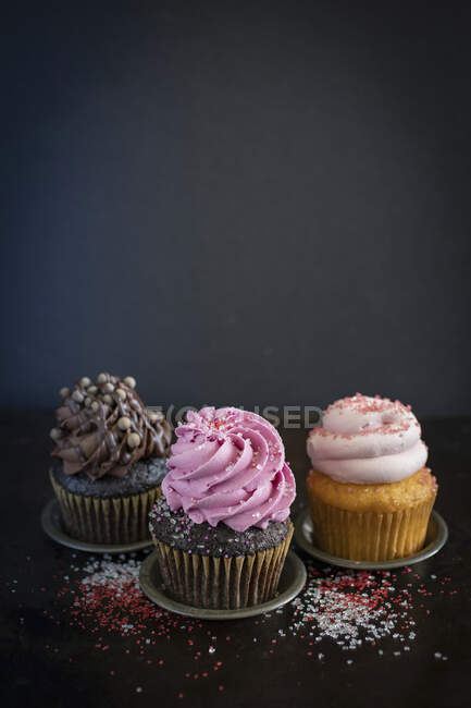 Drei verschiedene Cupcakes auf dunklem Hintergrund — Stockfoto