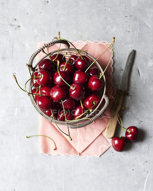 Fresh cherries in wire basket and on concrete surface with knife — Stock Photo