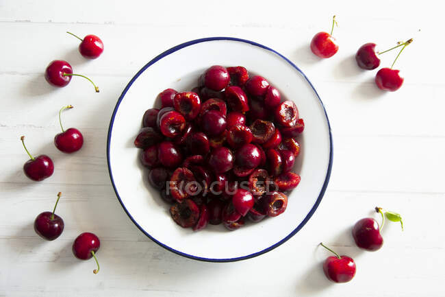 Enamel bowl of pitted cherries and whole cherries on table — Stock Photo