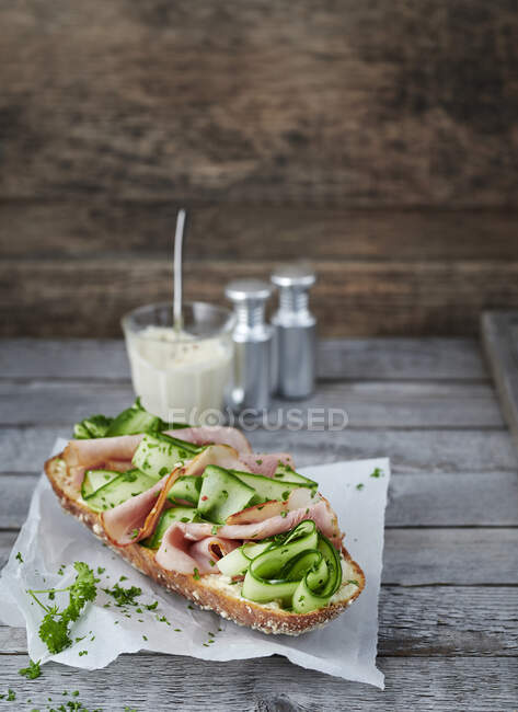 Baguette topped with cucumber and bacon on paper — Stock Photo