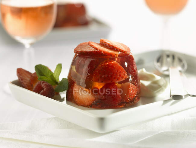 Jalea de fresa con rodajas de bayas frescas, menta y crema en el plato - foto de stock