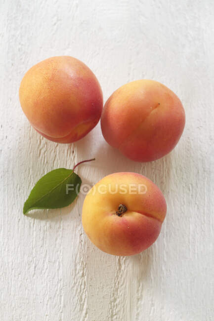 Drei frische Aprikosen mit grünem Blatt auf Holzoberfläche — Stockfoto