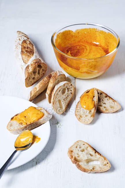 Rouille sauce in bowl and on sliced baguette with spoon on plate — Stock Photo