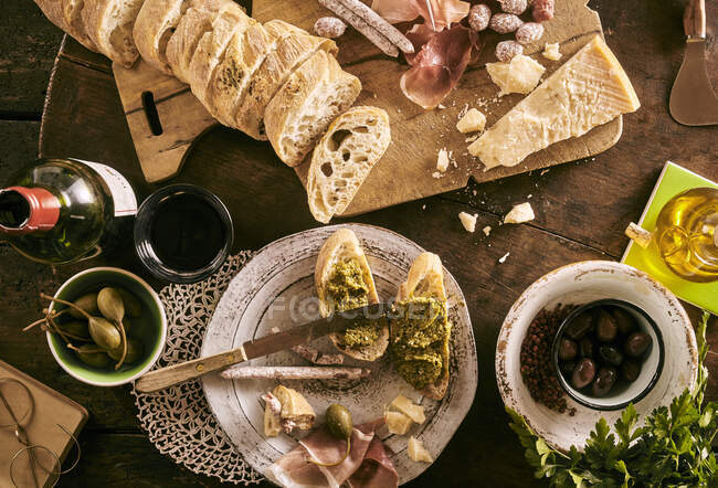 Bruschetta com pesto, mini salame, azeitonas, parmesão, azeite, alcaparras gigantes e vinho tinto — Fotografia de Stock