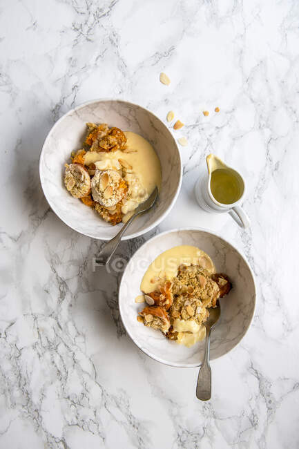 Apricot and almonds crumble desserts in serving bowls with custard cream — Stock Photo