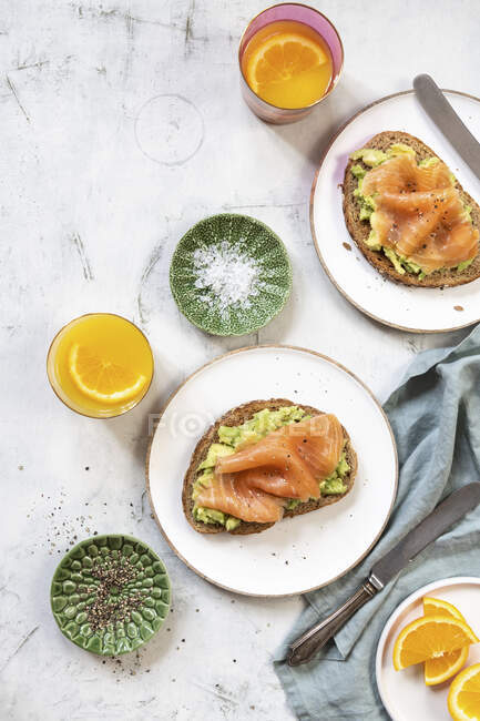 Fette di pane condite con avocado e salmone affumicato a colazione — Foto stock