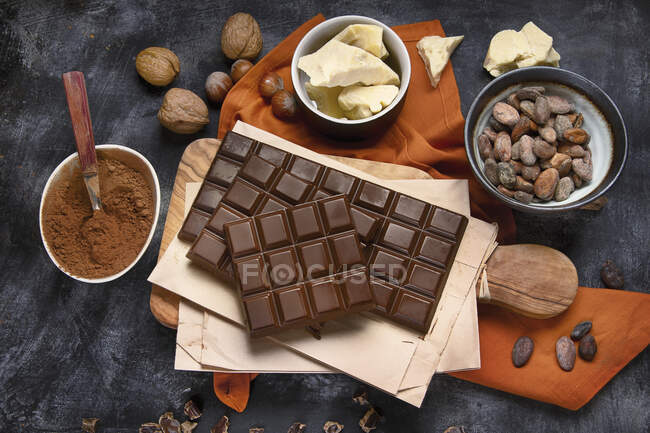 Barras de chocolate, cacao en polvo, mantequilla de cacao y frijoles de cacao sobre fondo negro - foto de stock