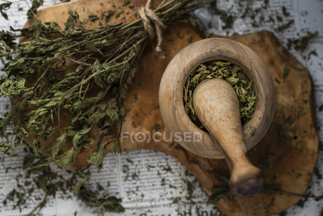 Menta seca en mortero de madera de olivo sobre tabla de madera en periódico - foto de stock