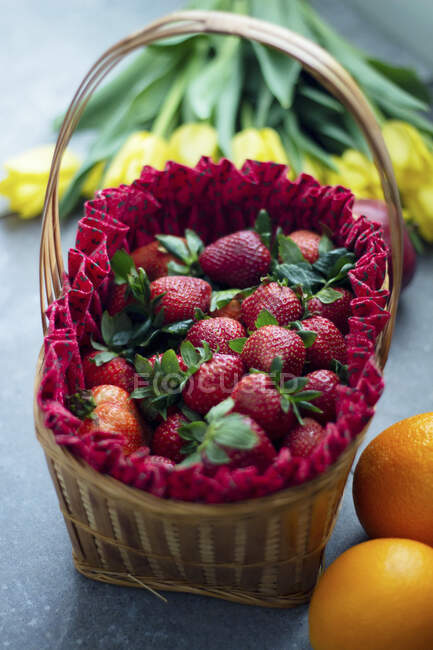 Erdbeeren im eleganten Korb mit rotem Tuch und Orangen auf dem Tisch — Stockfoto