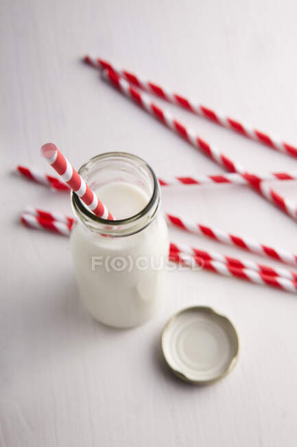 Una pequeña botella de leche y varias pajitas rojas y blancas - foto de stock