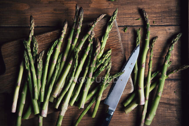 Espargos verdes com uma faca em uma superfície de madeira — Fotografia de Stock