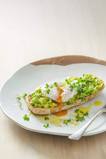Huevo escalfado en tostadas de ciabatta con aguacate machacado, berro y aceite de oliva - foto de stock