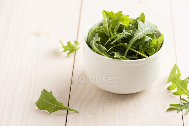 Fresh arugula in bowl on wooden table surface — Stock Photo