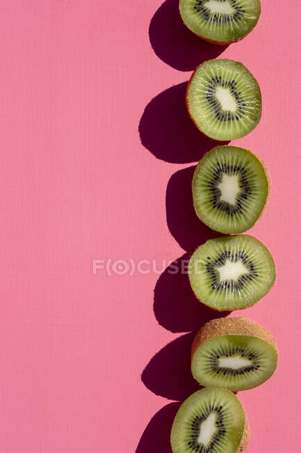 Une rangée de kiwis moitiés sur un fond rose — Photo de stock