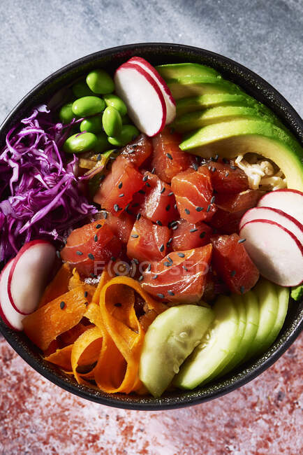 Poke bowl from overhead with gray stone surface on top and red mottled surface below — Stock Photo