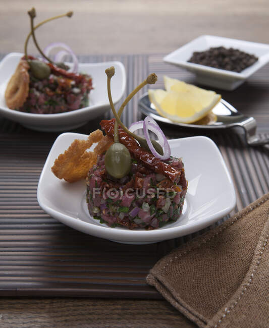 Tartare with capers, bread chips, onions and dried tomatoes — Stock Photo
