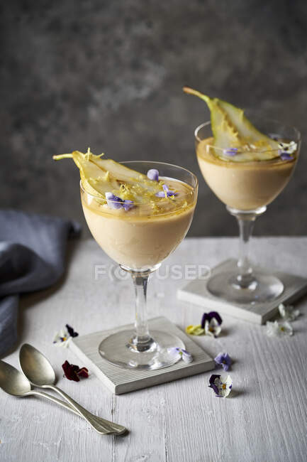 Pear custard desserts with edible flowers in glasses — Stock Photo