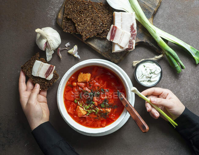 Borsch, Red beetroot soup, with girls hands, russian and ucranian food, green fresh onion and pork belly — Stock Photo