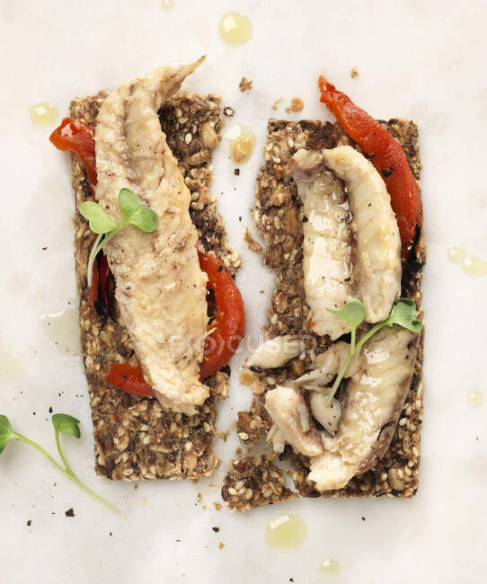 Mackerel filets on seed crackers with roasted red peppers and micro greens — Stock Photo