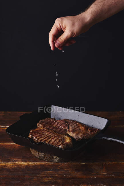 Male hands adding salt to beef steak on grill — Stock Photo