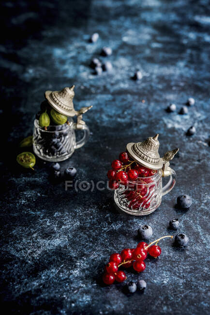 Red currants, blueberries and gooseberries in small cups — Stock Photo