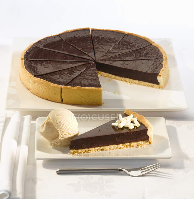 Torte au chocolat pour douze portions dans un étui à pâtisserie avec une cuillère de crème glacée vanille — Photo de stock