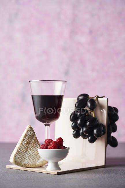 Vino tinto, uvas, queso y frambuesas frescas - foto de stock