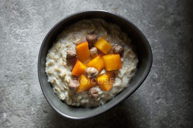 Porridge d'avoine roulé entier servi avec des kaki et des noisettes — Photo de stock