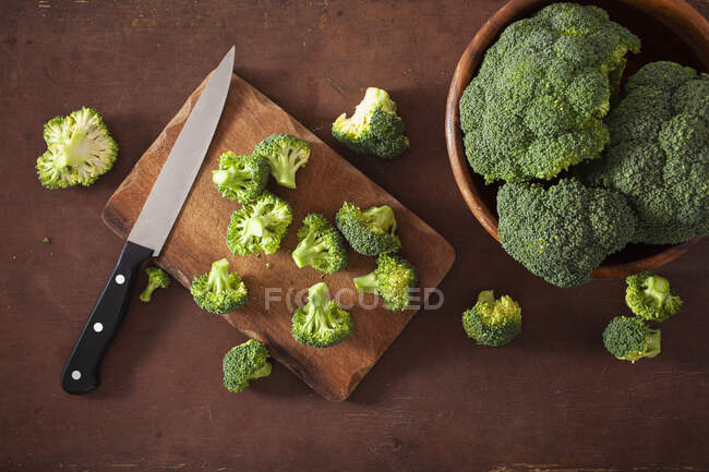 Fresh broccoli with a knife on a wooden chopping board and in a bowl — Stock Photo