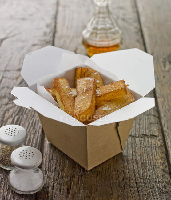 Una porzione di patatine, in una scatola di cartone da asporto, con sale marino — Foto stock